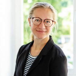 lächelnde blonde Frau mit Brille im schwarzen Blaser