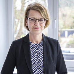 lächelnde blonde Frau mit schwarzer Brille im schwarzen Blaser